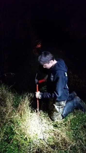 A man kneeling down in the grass with an axe.