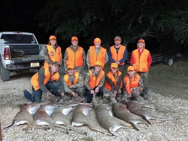 A group of people in orange vests standing next to dead animals.