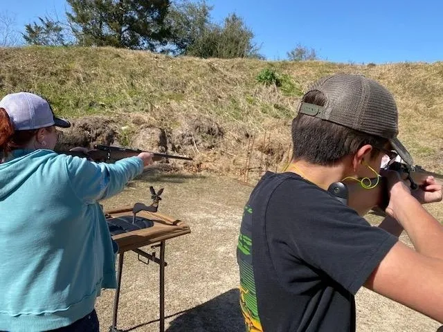 A man and woman shooting guns at an outdoor range.