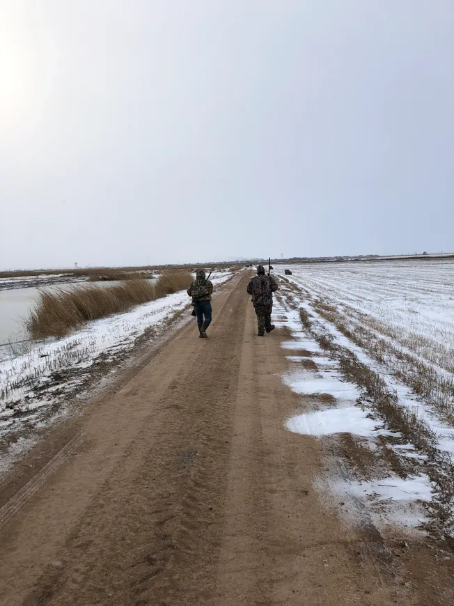 Two people walking down a dirt road in the snow.