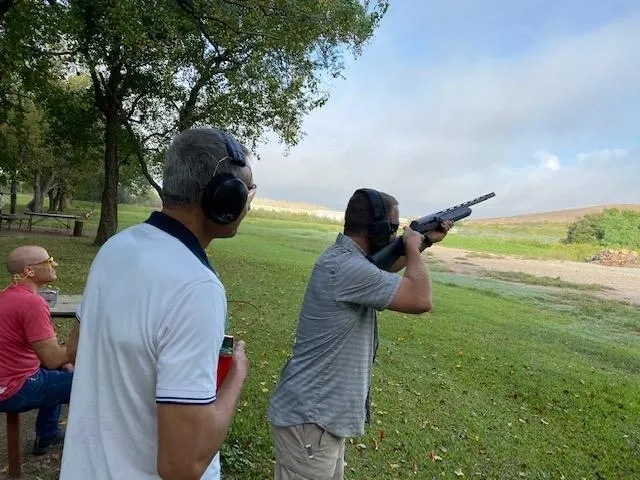 Two men are shooting guns in a field.