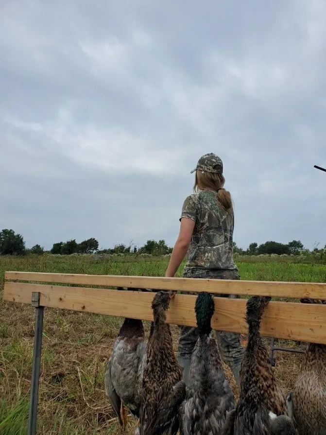 A woman in camouflage standing on top of a wooden bench.