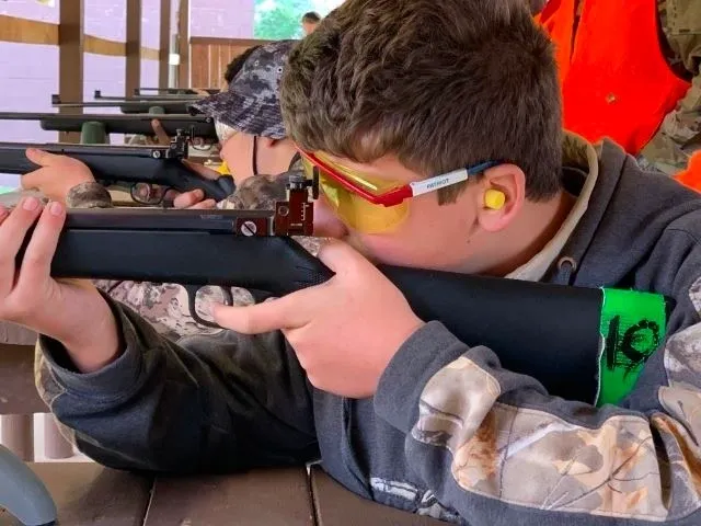 A young man is holding his rifle and aiming it.