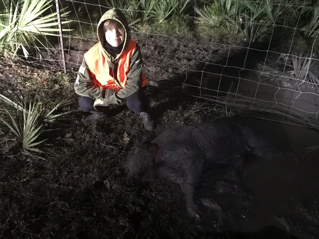 A man kneeling down in the dirt near a fence.