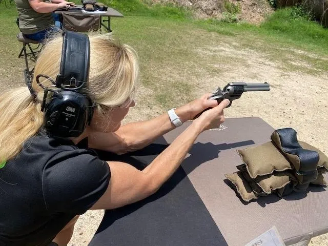 A woman is holding a gun and wearing ear muffs.