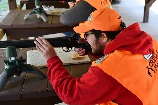 A man in an orange jacket is holding a rifle