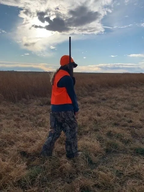 A man in an orange vest is walking through the field.