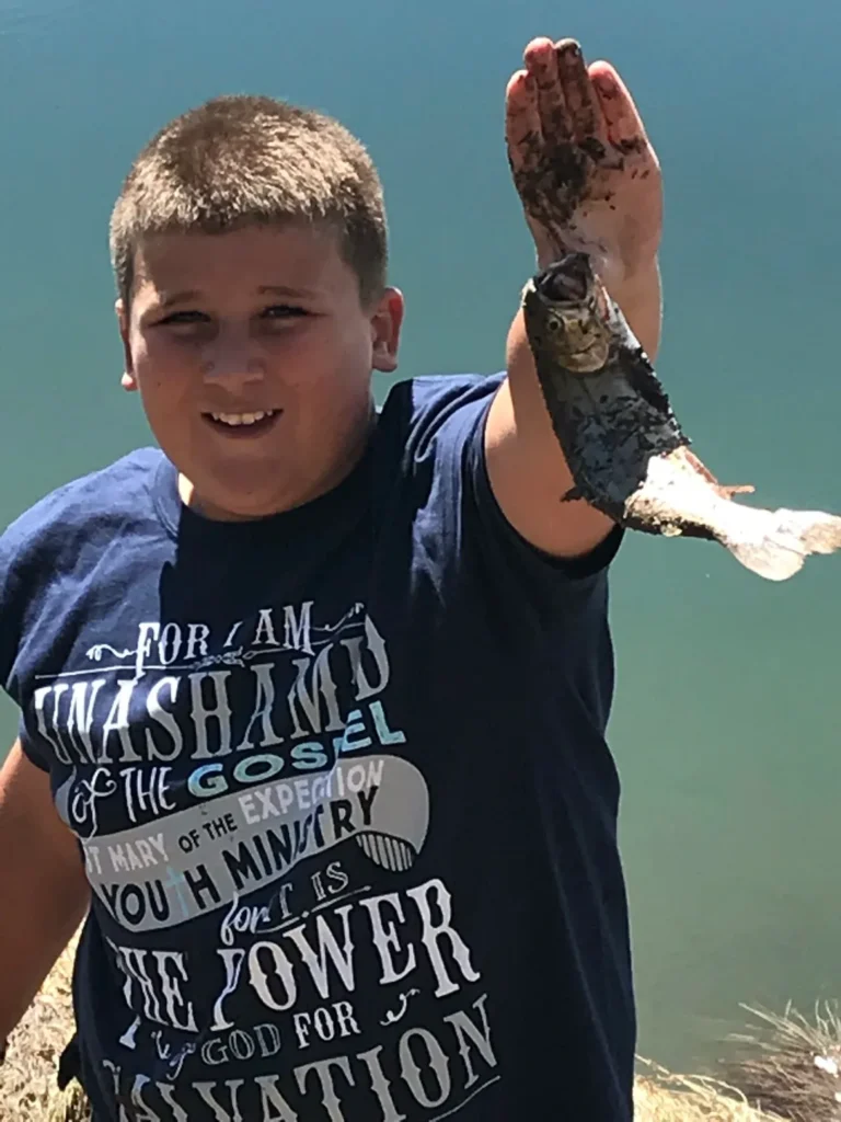 A boy holding fish in his hand and smiling.
