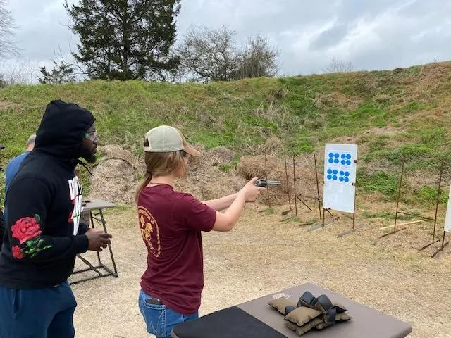 A woman is holding a gun and pointing it at the target.