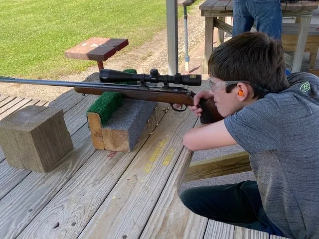A boy is sitting on the ground with a rifle.