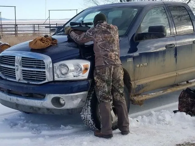 A man in camouflage is fixing the tire on his truck.
