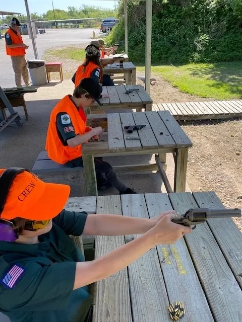 A group of people with guns sitting at picnic tables.
