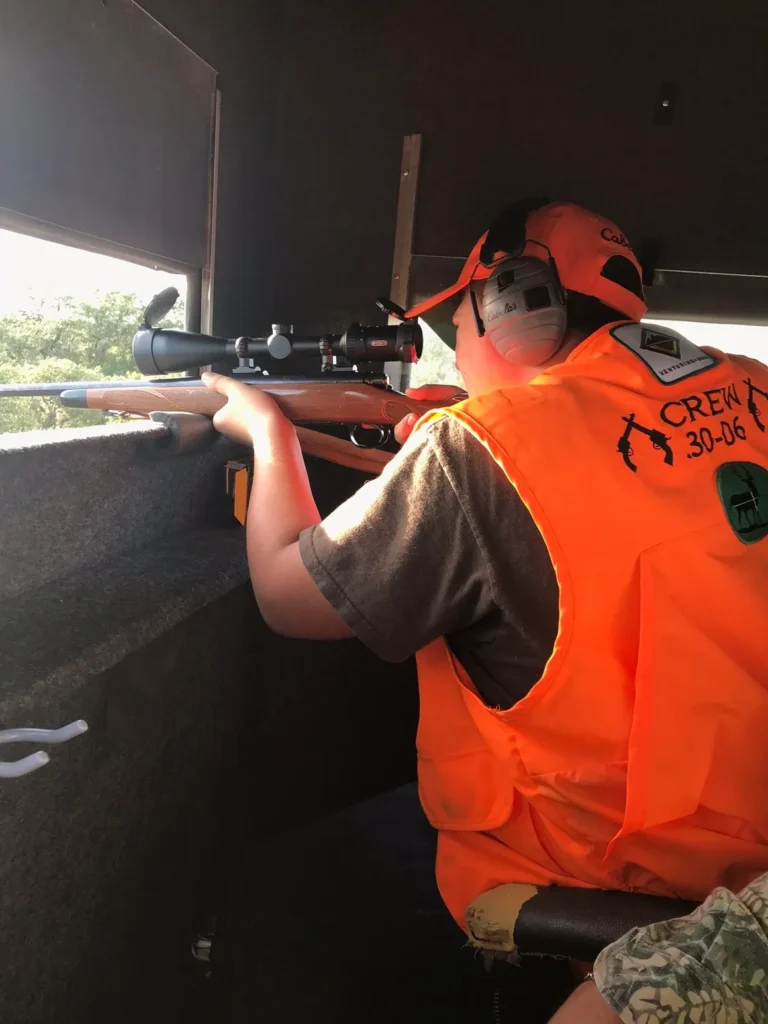 A man in an orange vest is holding a rifle