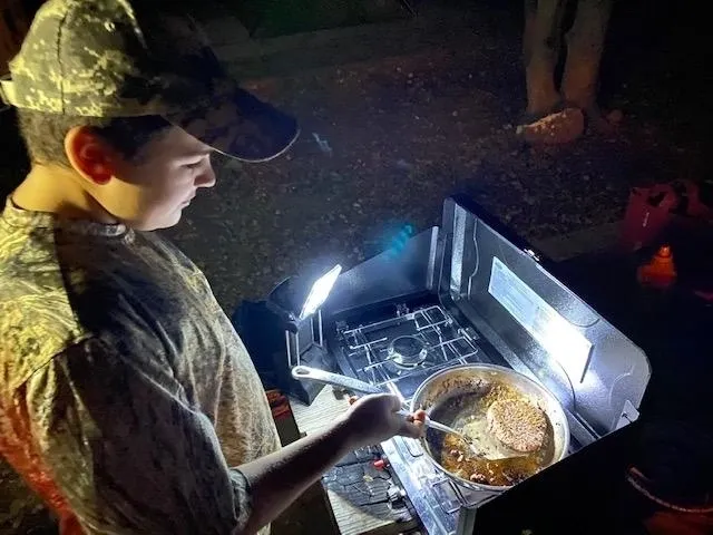 A man in camouflage cooking food on an outdoor grill.