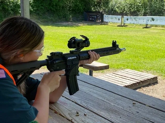 A girl is holding an ar-1 5 rifle on the bench.
