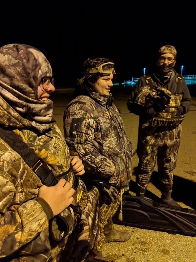 Three men in camouflage gear standing on a beach.