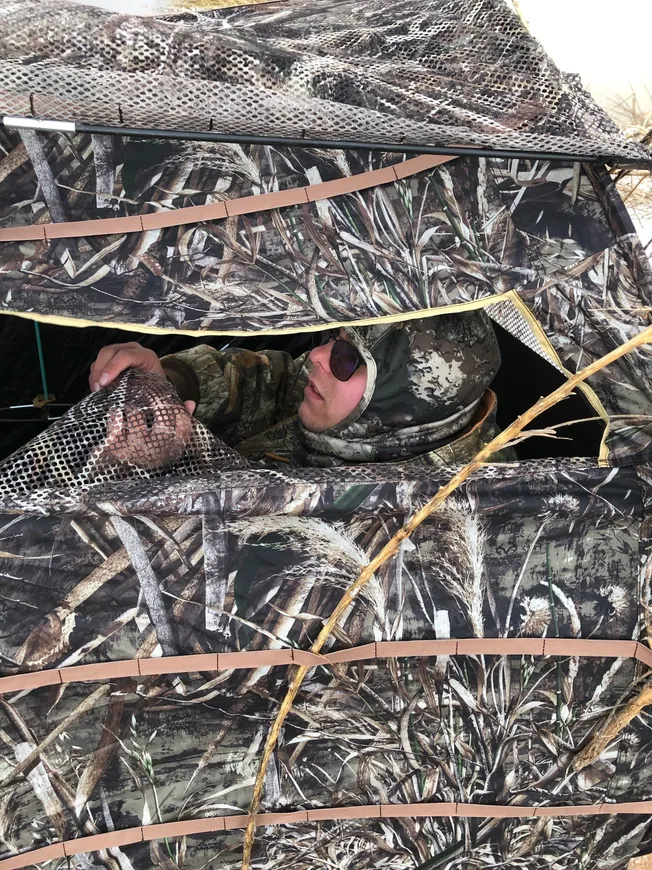 A man in camouflage hiding from the camera.