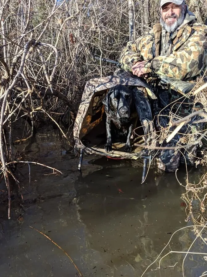 A black dog in the water with a camouflage cover.