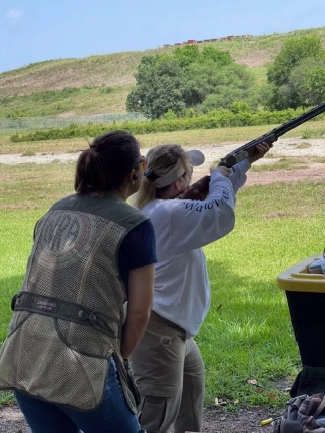 Two women are holding a rifle and aiming it.