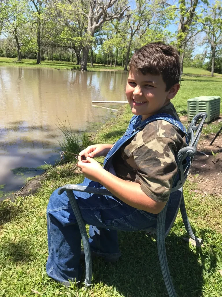A boy sitting on a chair near the water.
