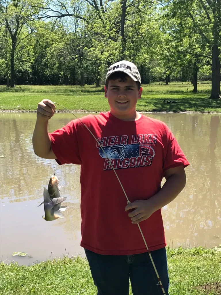 A boy holding a fish in his hand while standing next to the water.