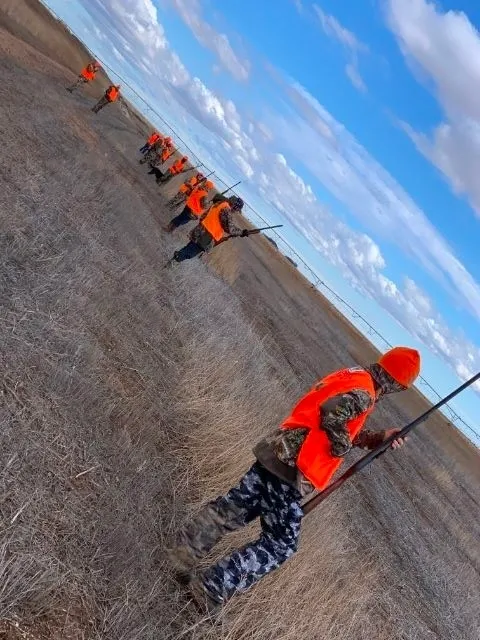 A group of people in orange vests standing on top of a dirt field.