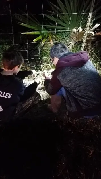 Two people are sitting in the dirt near a fence.