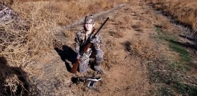 A woman kneeling down holding a rifle in her hand.