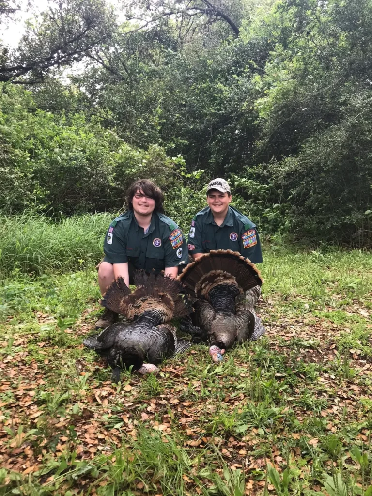 Two people posing with turkeys in a field.