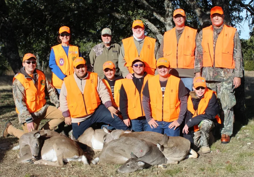 A group of people in orange vests standing next to deer.