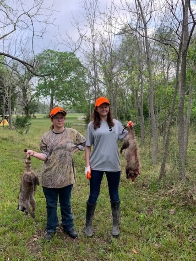 Two women holding dead animals in a field.