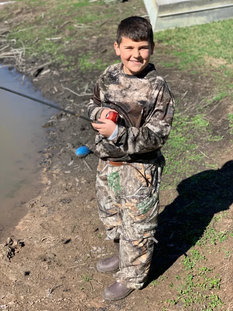 A young boy in camouflage holding a fishing rod.