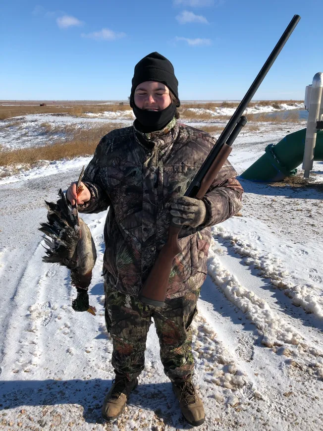 A man holding a fish and a rifle in the snow.