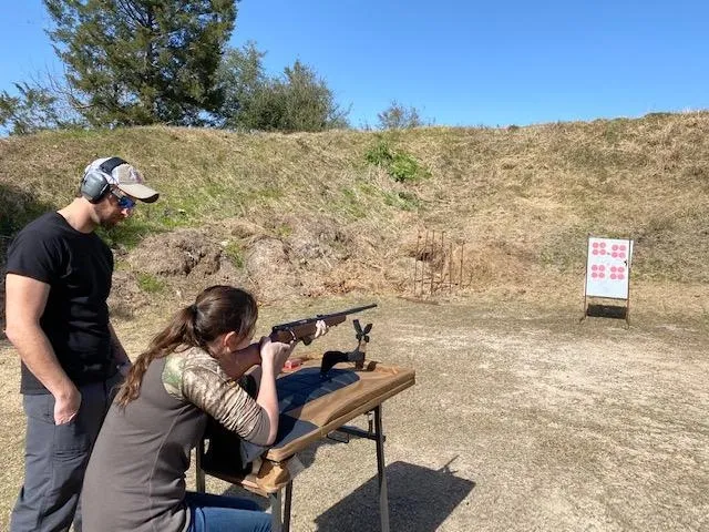 A woman and man are shooting guns at an outdoor range.