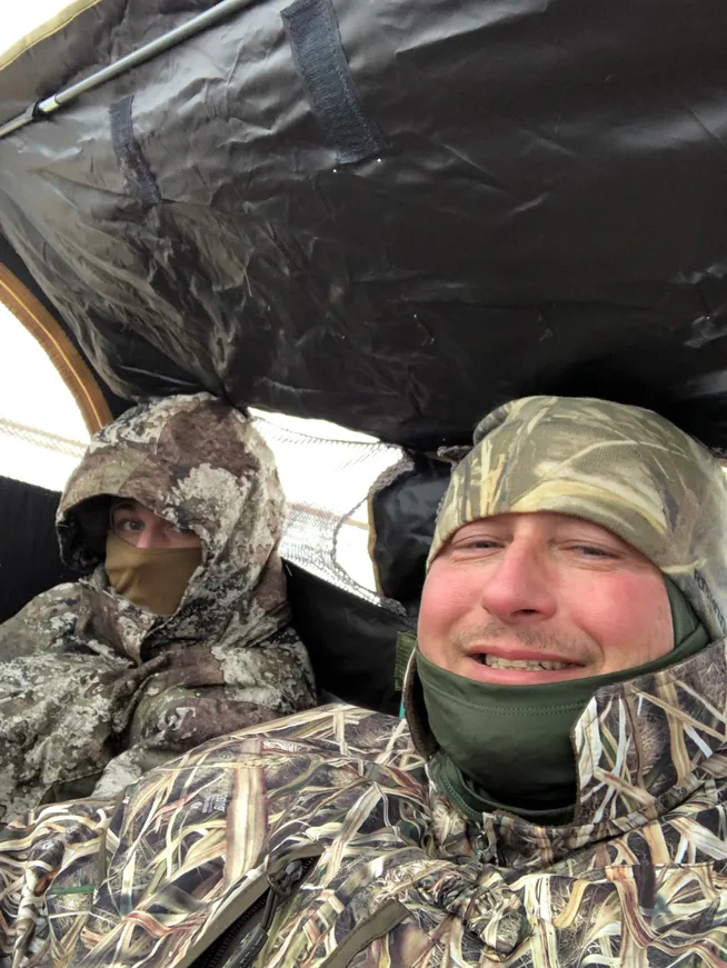 Two people in camouflage gear under an umbrella.