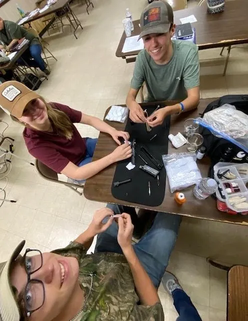 Three people sitting at a table with some bags of supplies.