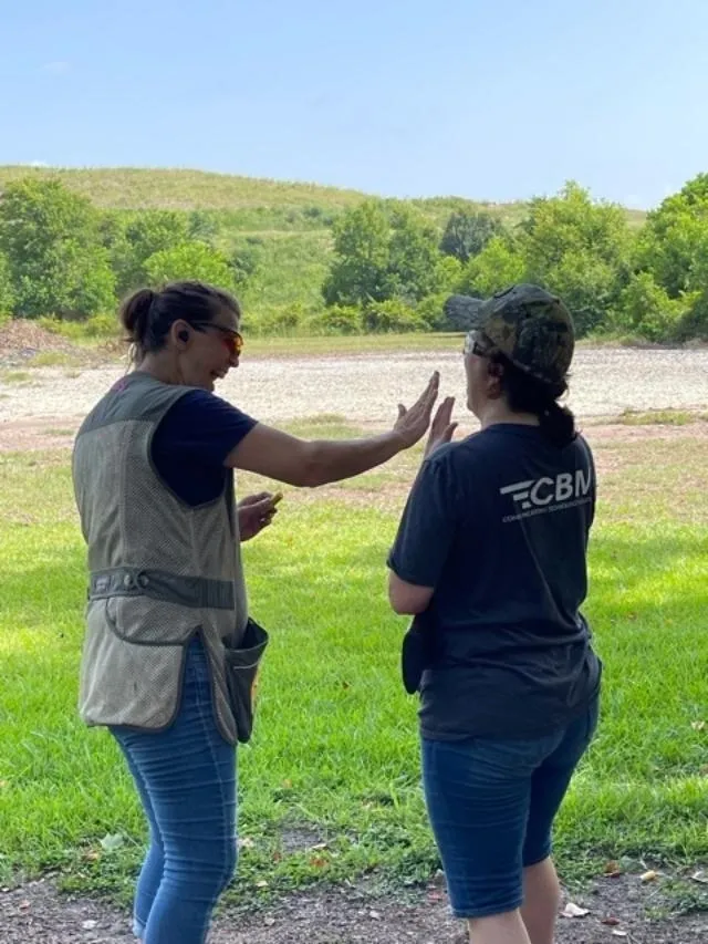 Two women are standing in a field with guns.