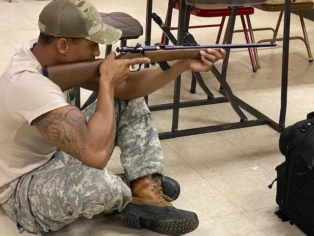 A man in fatigues sitting on the ground holding a rifle.