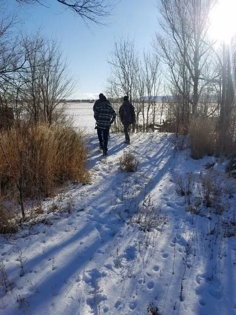 Two people walking in the snow near a body of water.