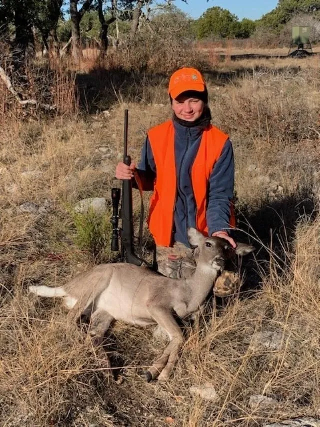 A man in an orange vest standing next to a goat.