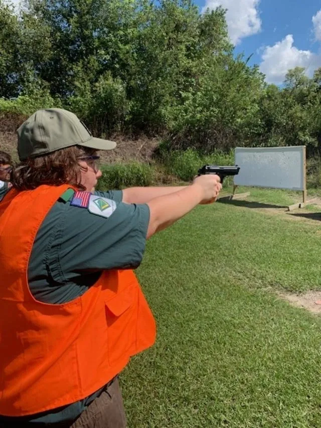 A man in an orange vest is holding a gun