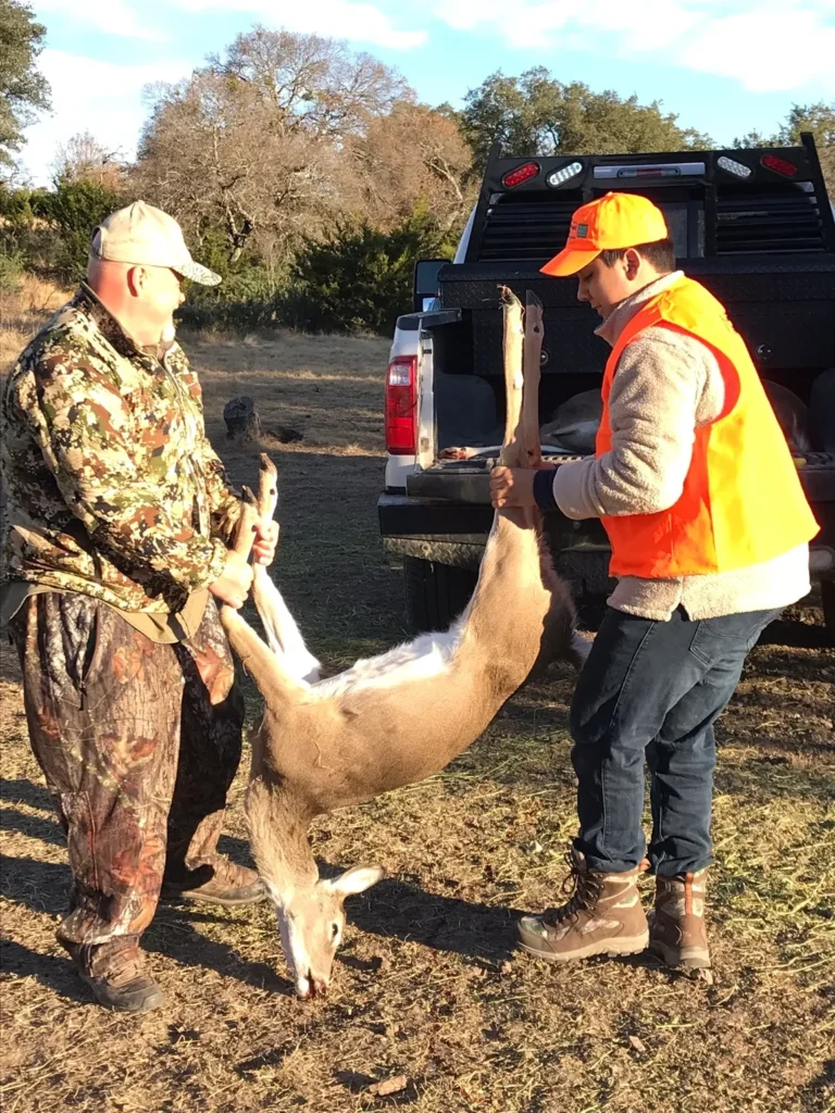 Two men in camouflage vests and orange hats are holding a deer.