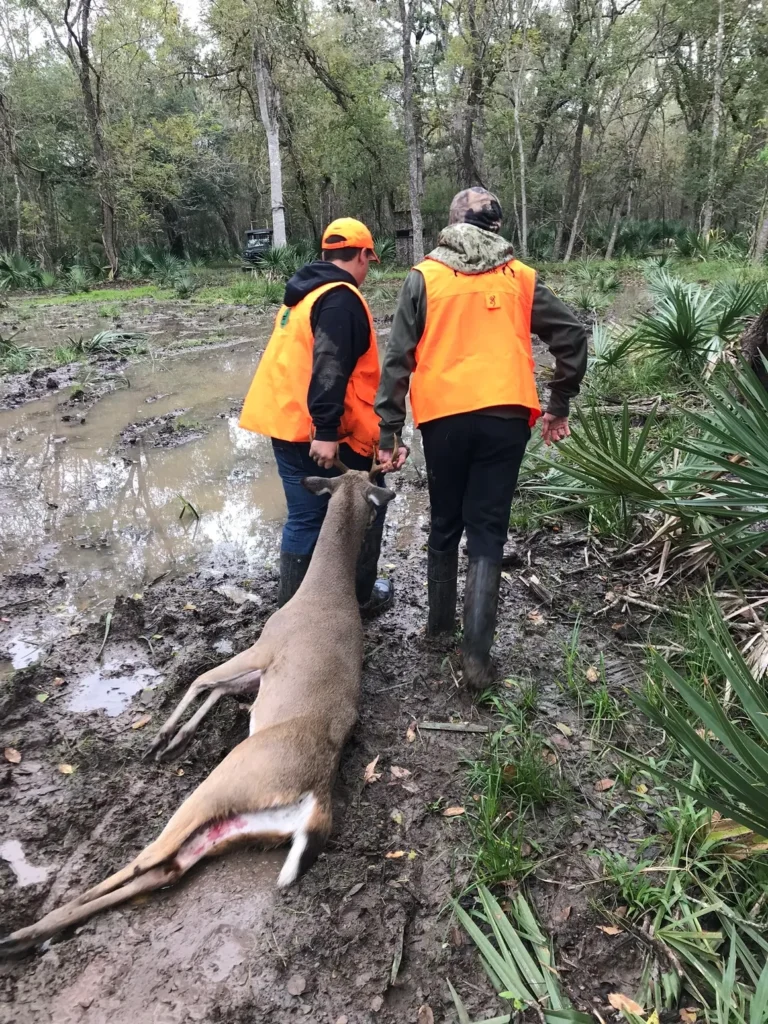 Two men in orange vests standing next to a dead animal.