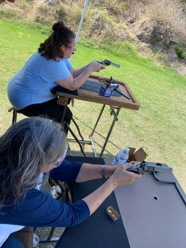 Two women sitting at a table with guns.