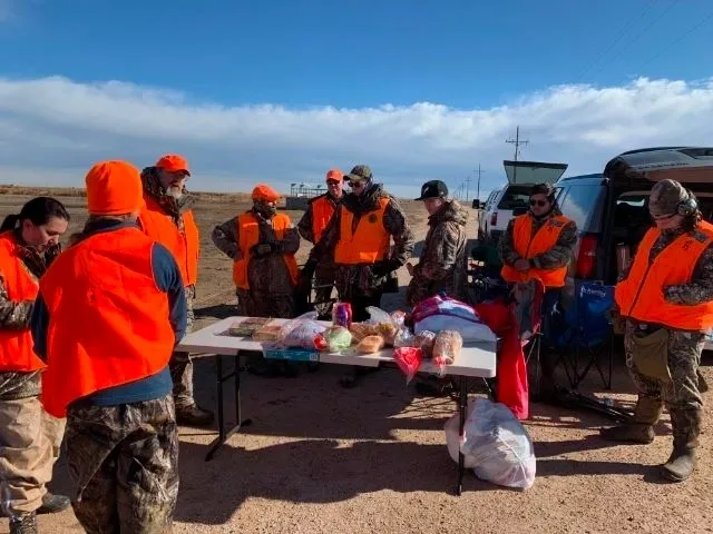 A group of people in orange vests standing around a table.