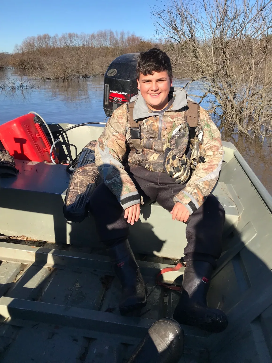 A boy in camouflage sitting on the back of a boat.