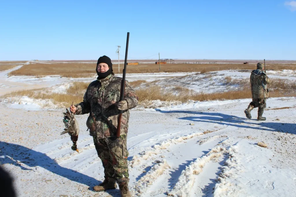 A man in camouflage holding two fish and a rifle.