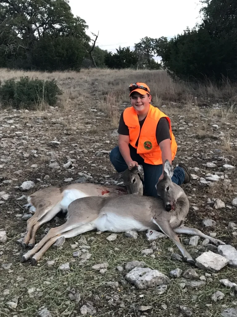 A man kneeling down next to a dead deer.