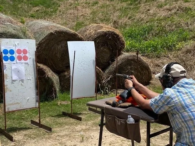 A man sitting in front of hay bales holding a gun.