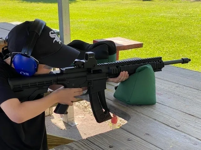 A person holding an ar-1 5 rifle on top of a wooden deck.